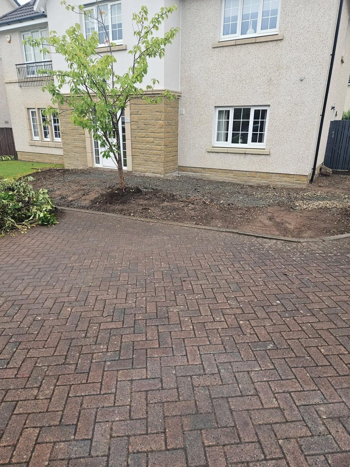 Wider view of the Dargavel frontage before work, showing builder's stone, bare soil and prunings piled at the lawn edge