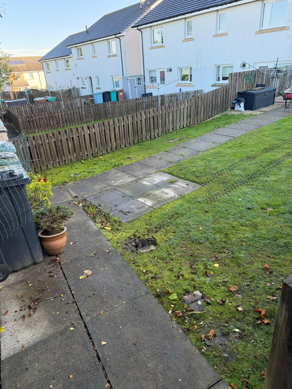Mossy, rutted back lawn in Chapelhall beside a slab path, with leaf litter and access chambers sitting in the wet grass