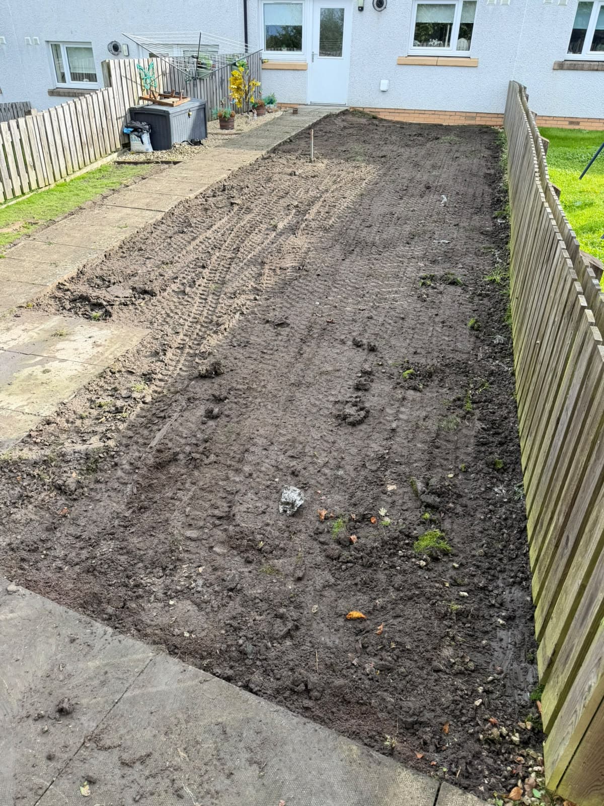 The Chapelhall back garden dug out to bare soil between the slab path and the fence, with a level peg set in the ground