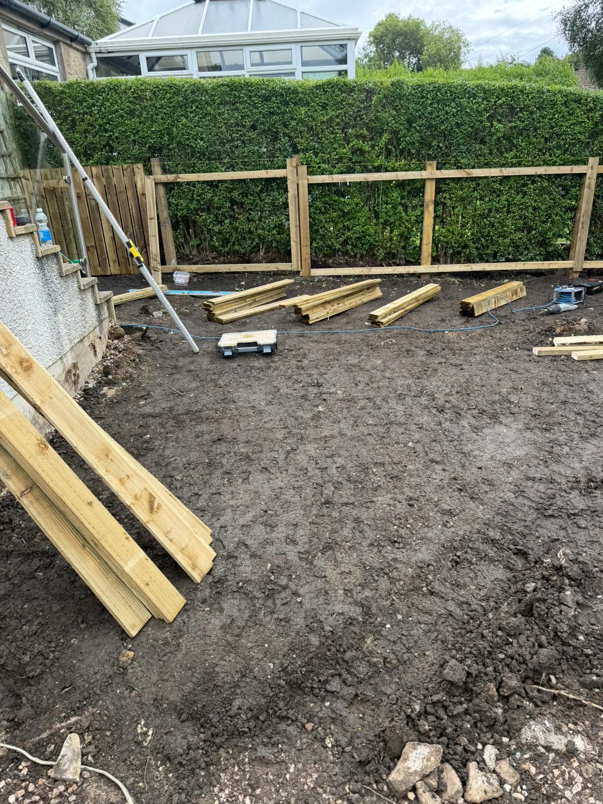Glasgow rear garden during clearance, stripped to bare soil with new fence posts and rails going in along the hedge line